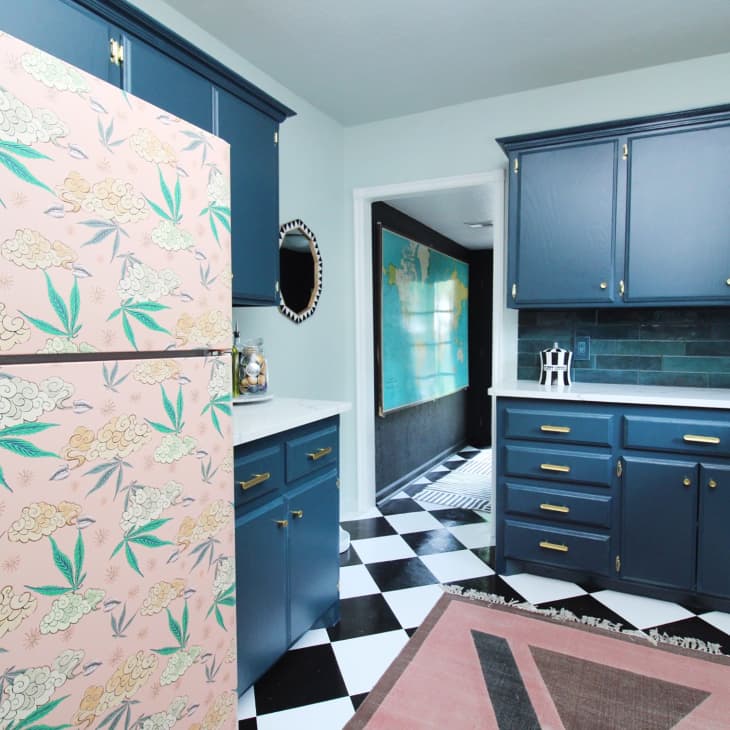 Kitchen with black and white checkered floor, blue cabinets, leaf-patterned pink fridge