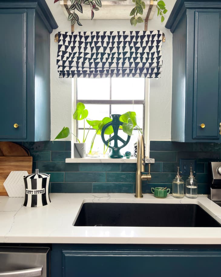 Kitchen sink area with blue cabinets, black peace sign in window with a black and white hearts curtain