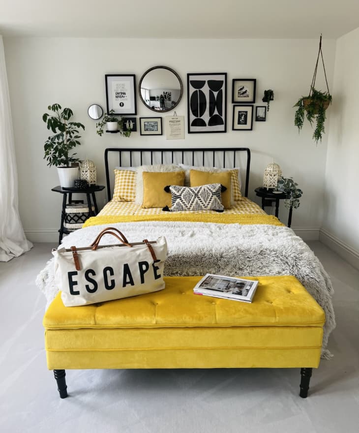 Black and yellow bedroom with black slotted bed frame, lots of framed photos displayed behind the bed.