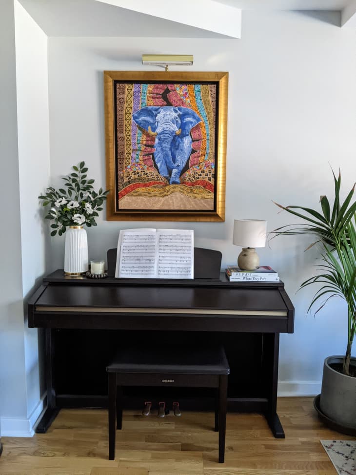Upright piano in living room with painting of elephant mounted on the wall above.