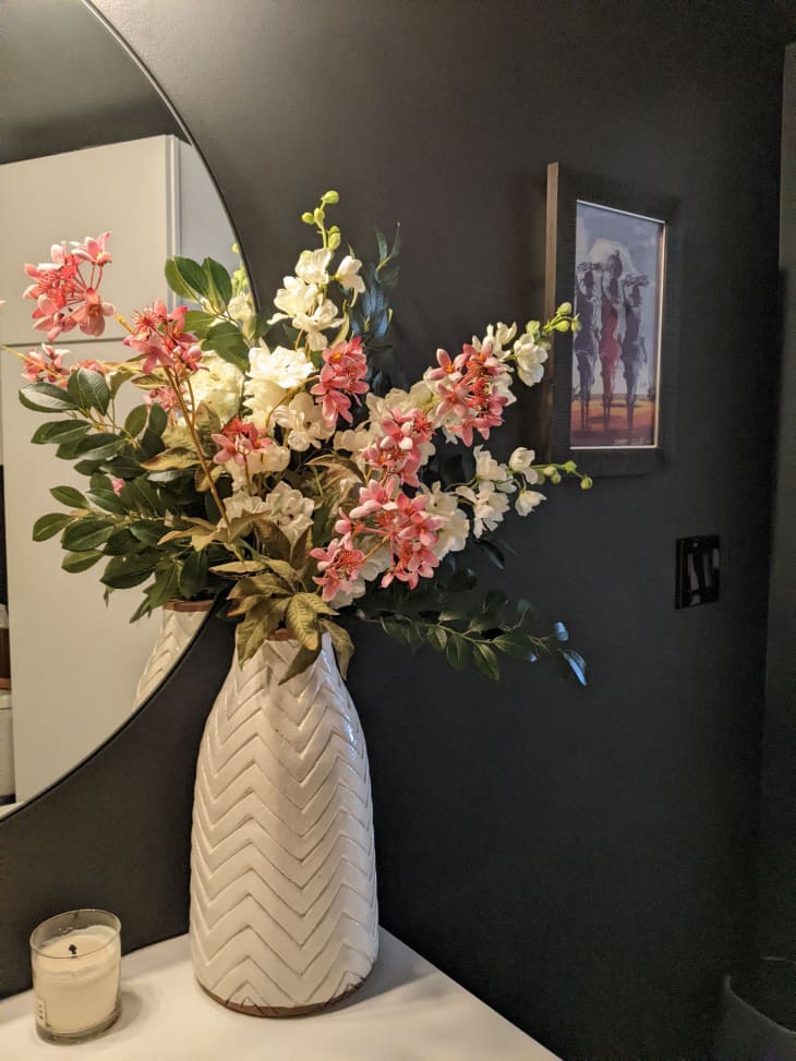 Dark colored bathroom with vase of flowers on vanity countertop.