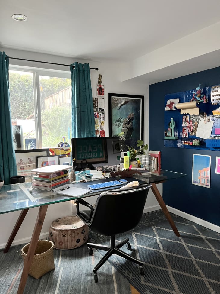 Home office/workspace with big window, one navy blue wall, large glass top desk with wood legs