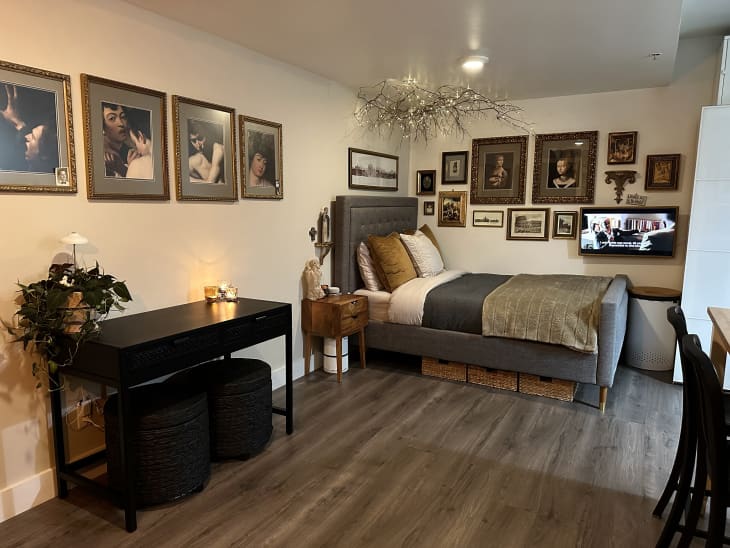 Apartment with lots of neutral, natural hues, Italian art, natural and black accents, This image shows the bedroom, with branches as a light fixture over the bed, gilt-frame portraits, bed with black brown and white bedding, framed closeups of caravaggio paintings