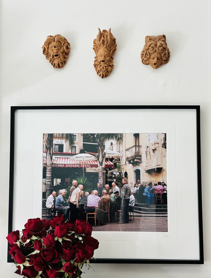 Apartment with lots of neutral, natural hues, Italian art, natural and black accents, classical-themed wallpaper. Detail of framed photo on wall, small versions of classical fountain sculptures mounted on wall, vase of red roses