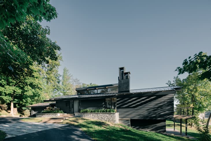 Mid-century modern house exterior that's painted black and featured stone retaining wall.