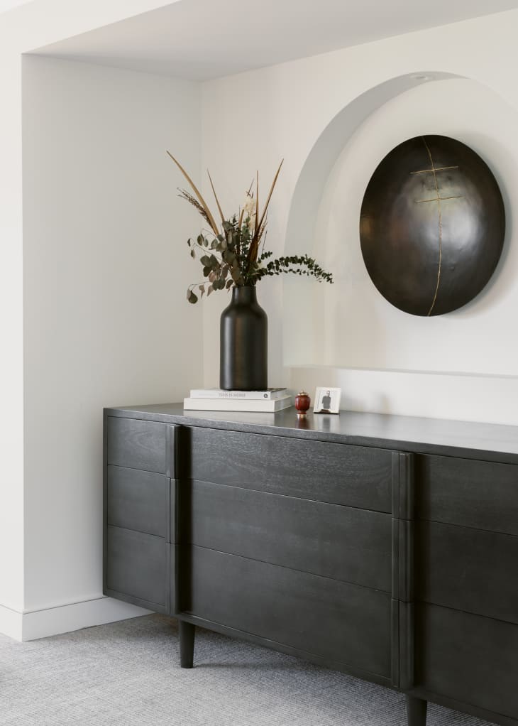 Corner nook with an arched inset of the wall with a large round black art piece hanging within the inset, above a black wood modern credenza.