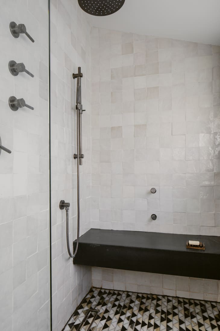 Contemporary bathroom walk-in shower with glossy white zellige wall tiles, Art Deco-inspired geometric triangle floor tile, and a sleek black shower ledge.