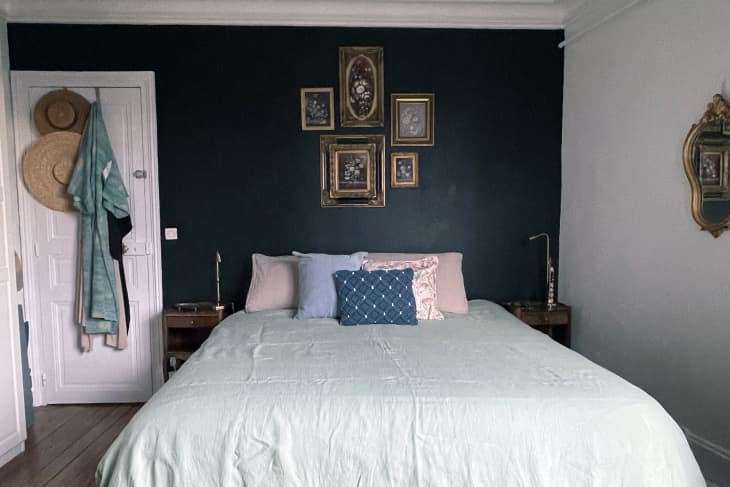 bed with pale green linens, pink and blue pillows, small deep blue gallery wall of vintage floral framed art, wood bedside tables