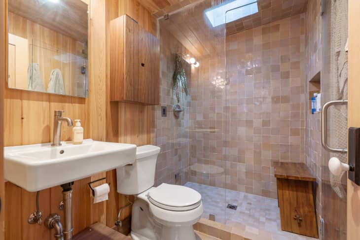 Wood paneled bathroom with neutral colored tiled in glass doored shower.