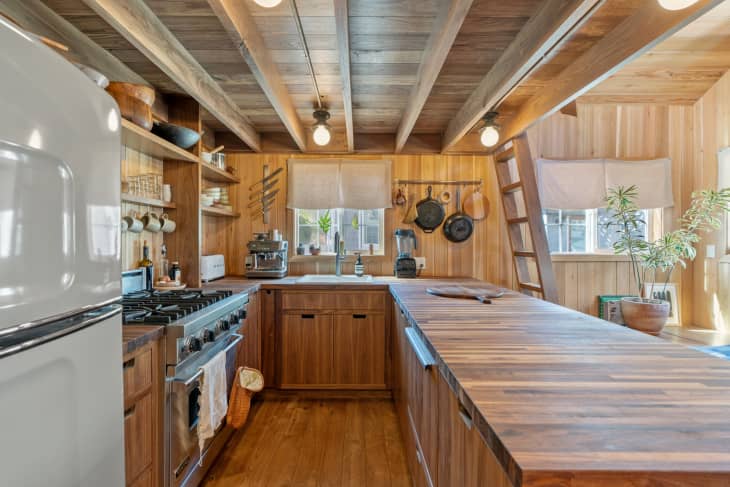 Wood paneled kitchen with vintage lighting with   tulip-like silhouettes. Cookware hung in along walls in kitchen.