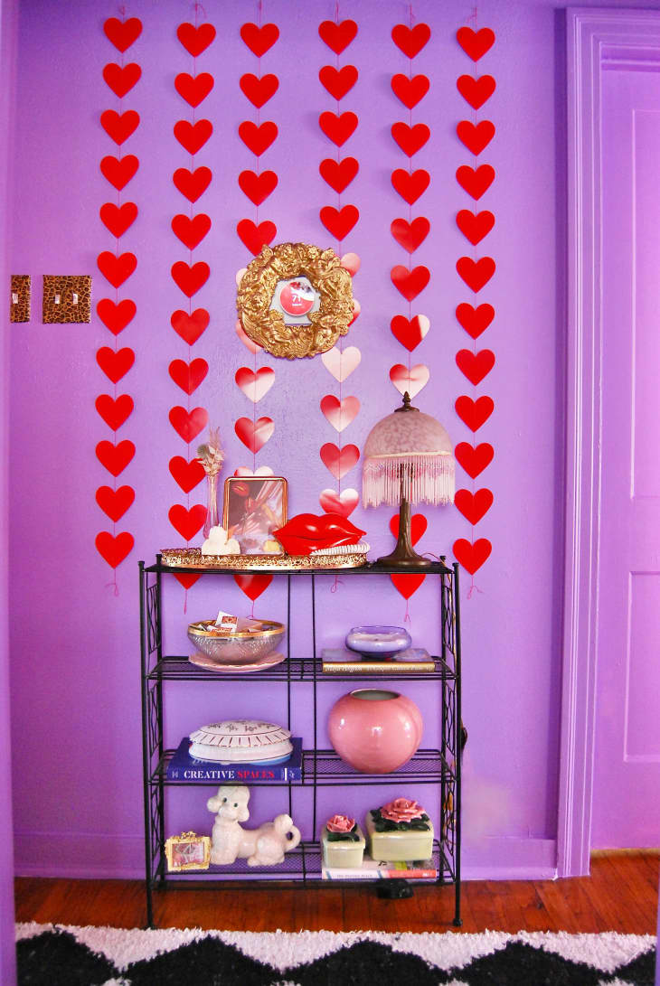 Detail of small shelves with decorative objects in lavender hallway with red hearts on wall, black and white harlequin shag rug