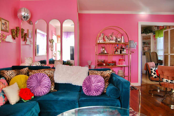 colorful living room with some pink walls, some white, pink front door, blue velvet sofa with colorful throw pillows, arched deco mirrors, lots of colorful framed wall art