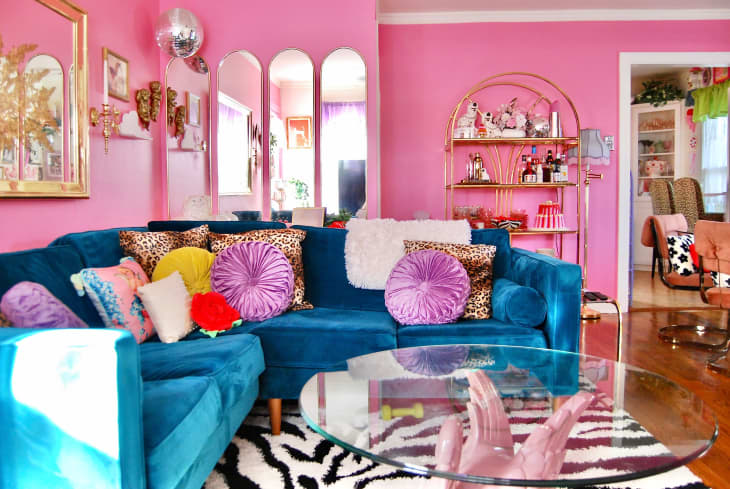 colorful living room with some pink walls, some white, pink front door, blue velvet sofa with colorful throw pillows, arched deco mirrors, lots of colorful framed wall art