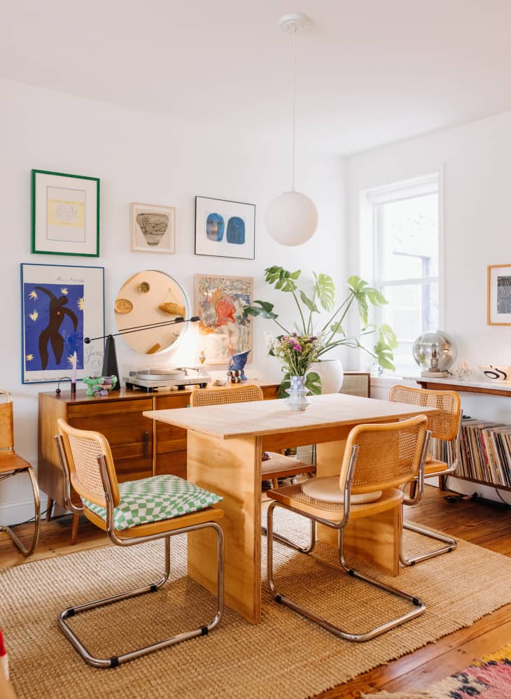 Philadelphia residence with white walls, lots of wood details: dining room with unfinished wood table, rattan back chairs, sisal rug, wood credenza with record player with gallery wall behind
