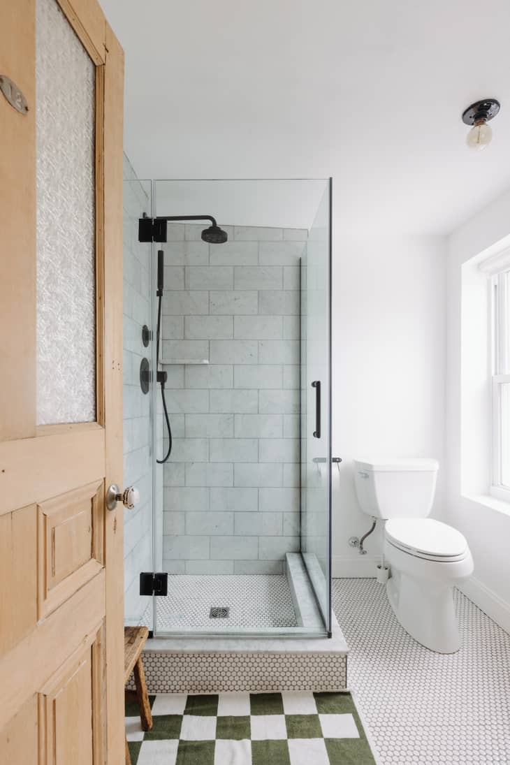 Philadelphia residence with white walls, lots of wood details: bathroom with light gray/white tiled shower with black hardware, checkered bath mat