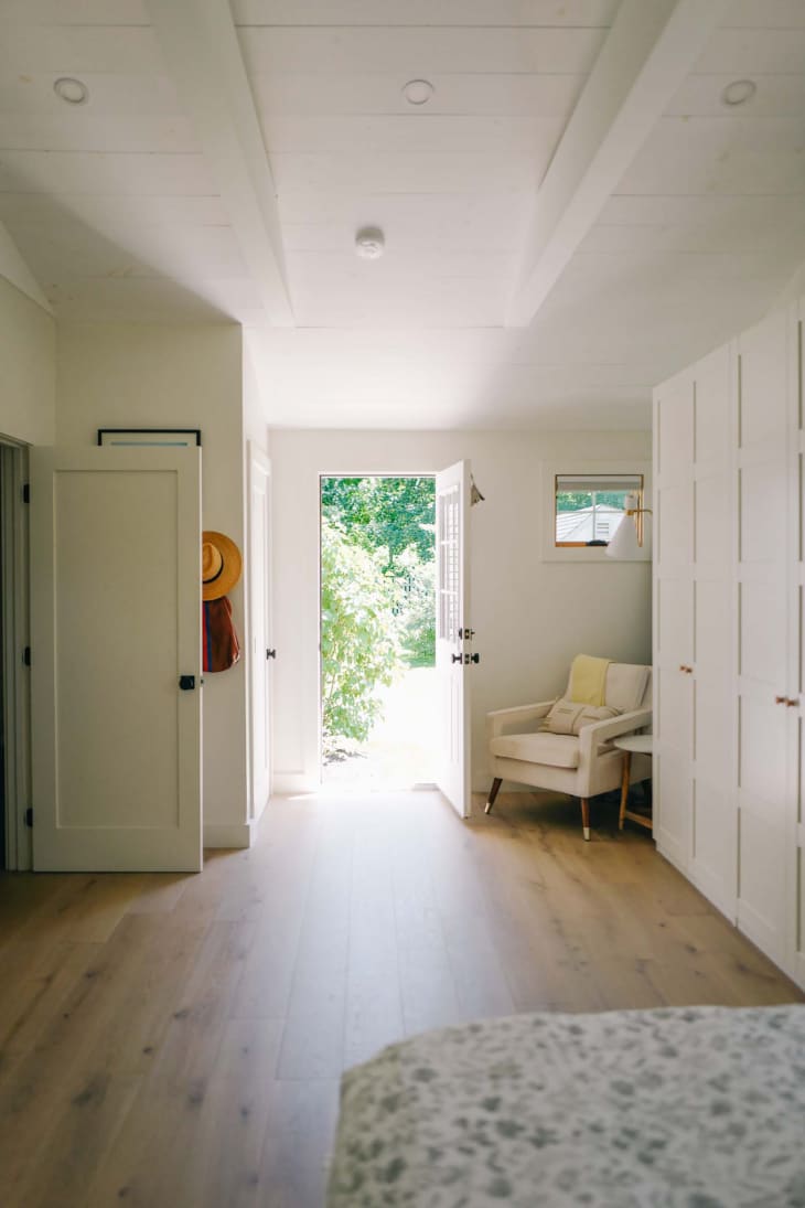 Door open in light colored bedroom with cream colored arm chair in the corner.