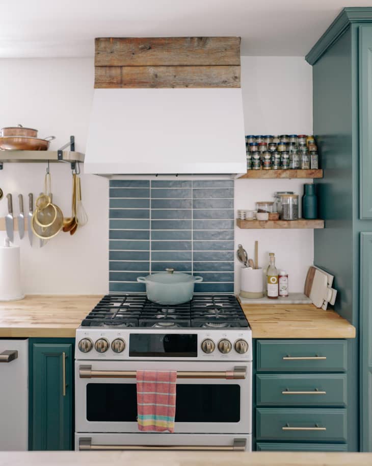 Newly renovated kitchen with blue/green colored cabinets with gold hardware and white gas stove.