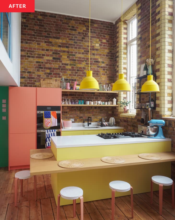 Kitchen after home renovation. Lots of exposed brick with different colored brick details around large windows, yellow cabinets, yellow pendant lights, coral pantry, wood bar projecting off island with coral and white barstools