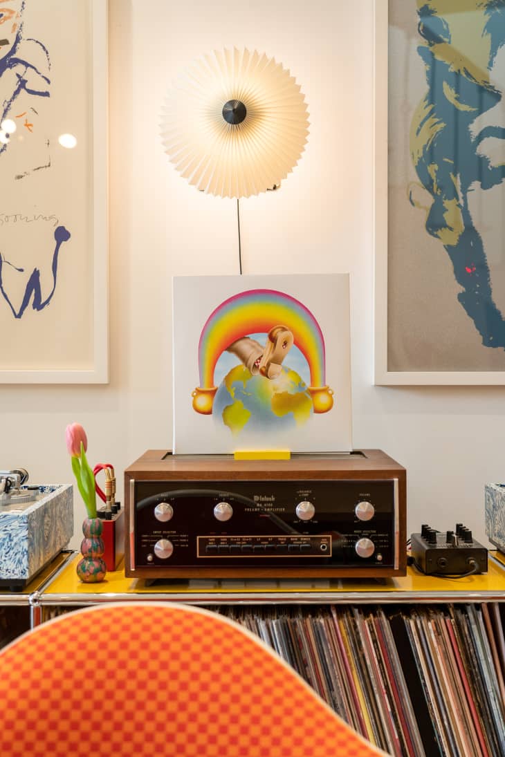 Stereo receiver on media console with lots of albums stored below. Parasol lamp and artwork above media center.