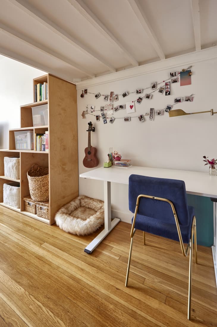 room with wood floor, wood bookcase/shelves with books, storage baskets, white walls, white beamed ceiling, white desk/table against wall with blue chair