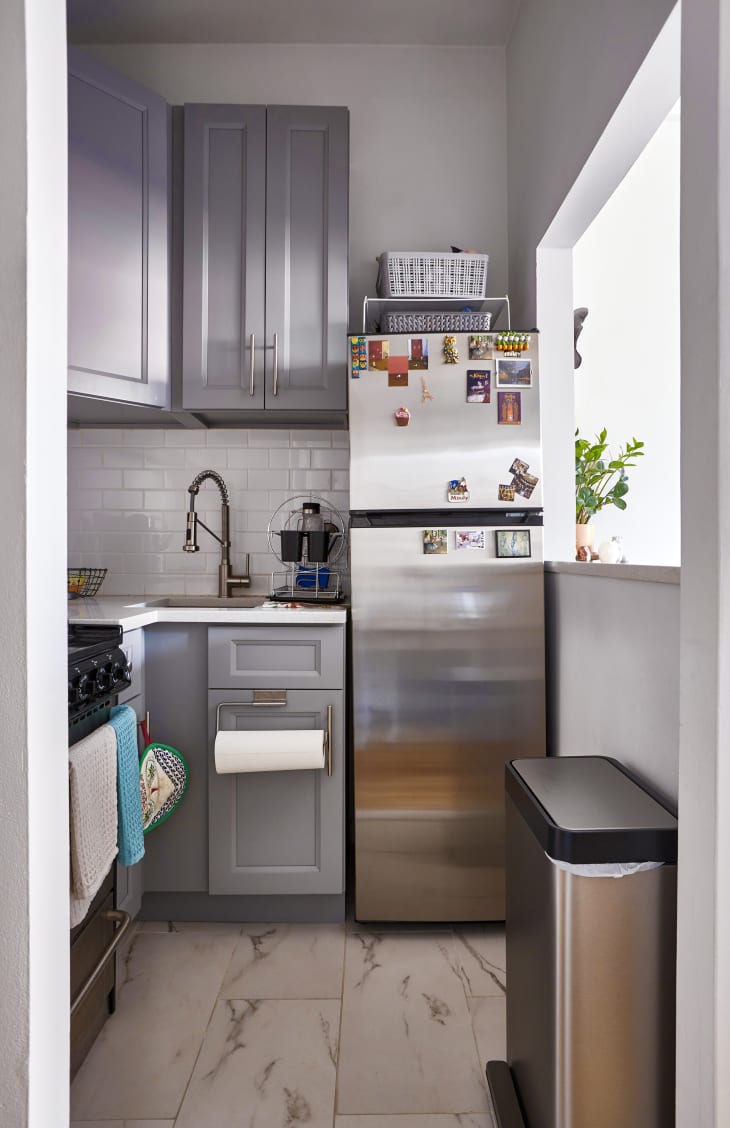 View into small kitchen with light gray painted cabinets, white walls, white subway tile backsplash, marble floor tiles