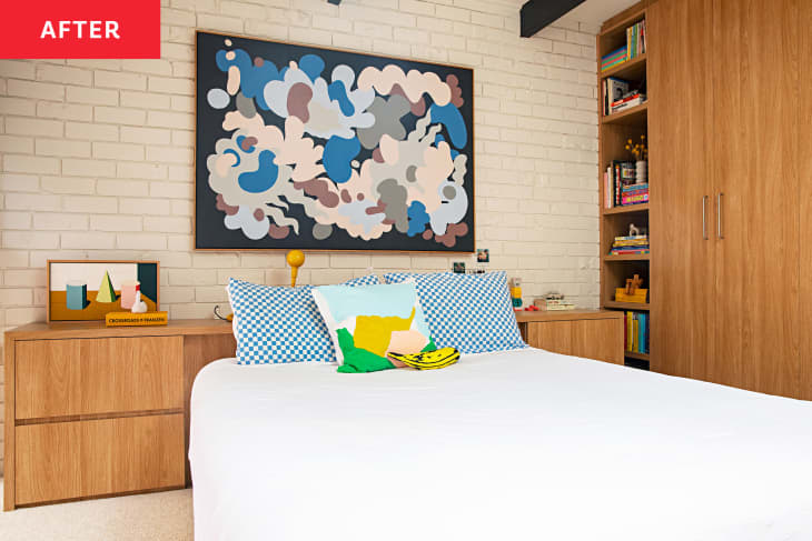 bedroom with painted white brick wall behind bed, white bed linens, Large wood closet and shelves on one wall, wood headboard with built-in side tables, art and throw pillows with blue accents