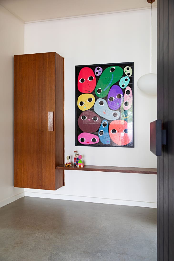 Entry way with tall wood cabinet, one floating shelf at bench level. Colorful art