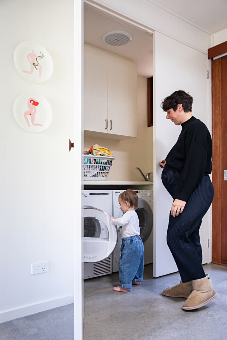 woman and toddler in laundry room/closet area. White walls and doors, white cabinets, basket of laundry