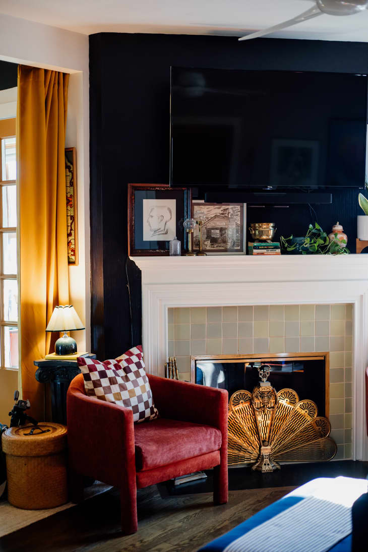 corner of living room with rust colored velvet accent chair, white fireplace with tiles, gold peacock fan