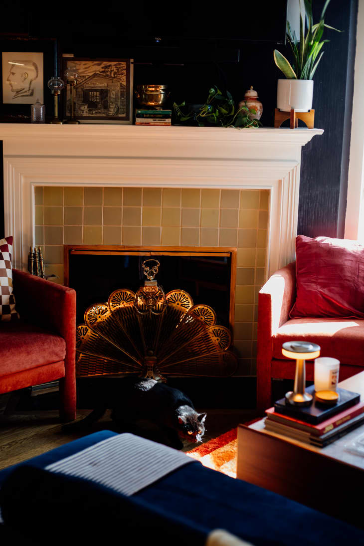 corner of living room with rust colored velvet accent chair, white fireplace with tiles, gold peacock fan