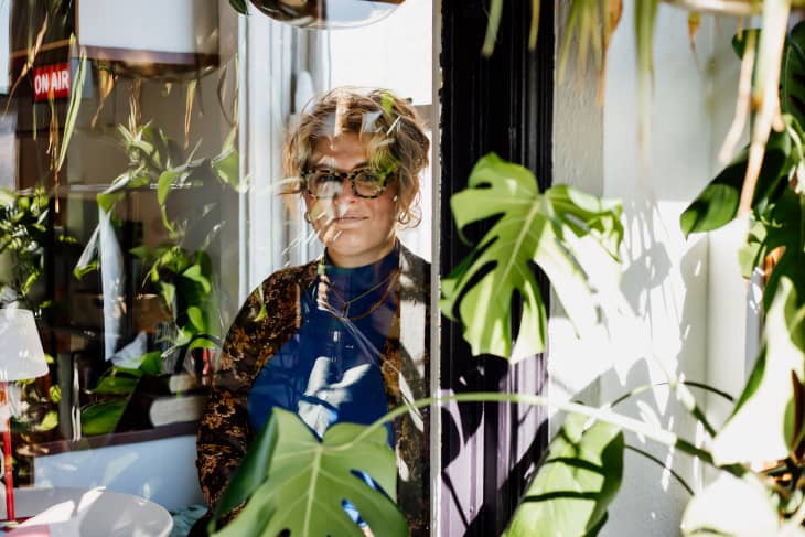 woman looking out the window through plants from her Chicago apartment