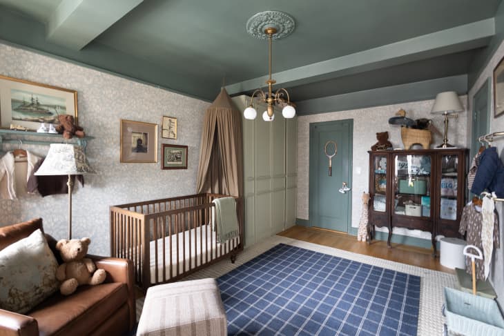 Leather armchair, dark wood crib next to wardrobe in room with floral wallpaper and blue-green ceilings