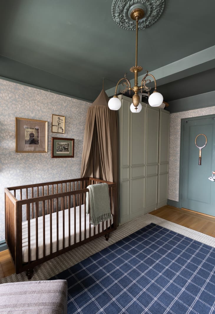 Dark wood crib next to wardrobe in room with floral wallpaper and blue-green ceilings