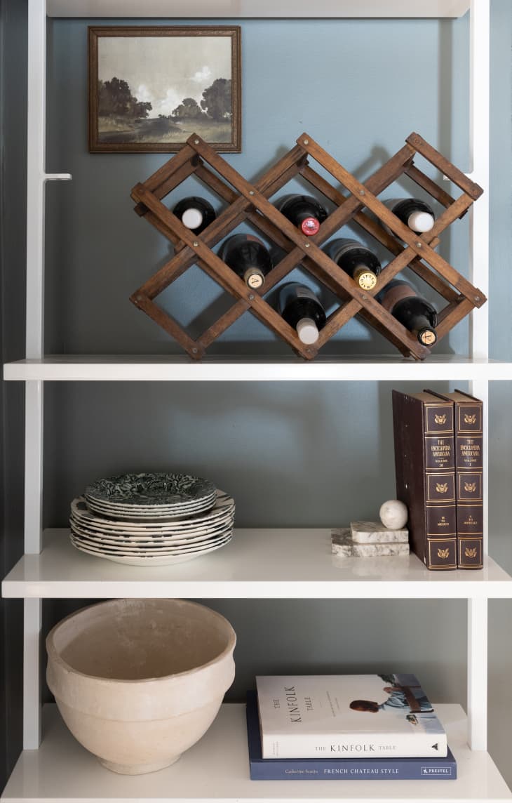 Wooden wine holder, plates, and books on white shelf