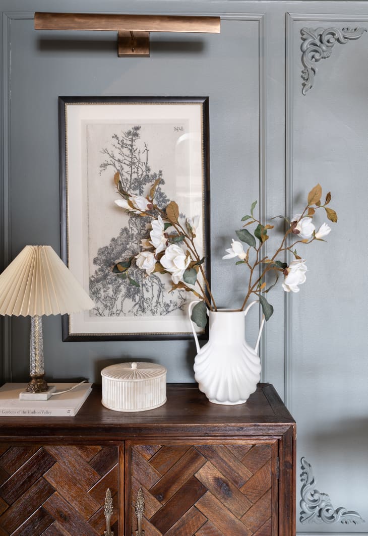 Wood sideboard against gray wall with art, vase and lamp