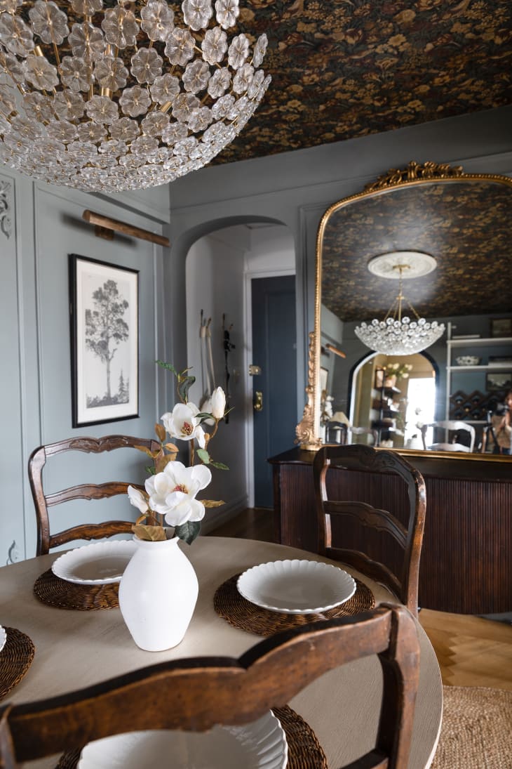 Wood table and chairs, large gold mirror, dark wood buffet, and chandelier in dining room with blue-gray wallpapered ceiling