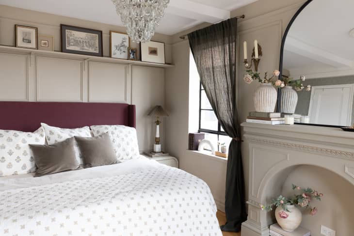Floral bedspread on uphostered frame in neutral bedroom with mirror above fireplace
