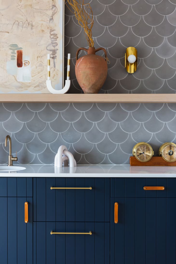 kitchen counter and sink with deep blue cabinets, white countertop, gold sink hardware, gray scalloped tile, wood shelf