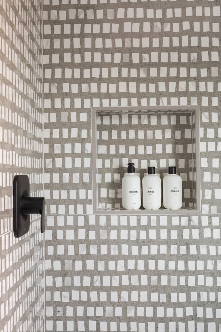 shower with gray and white pattern walls, small niche with bottles, black hardware