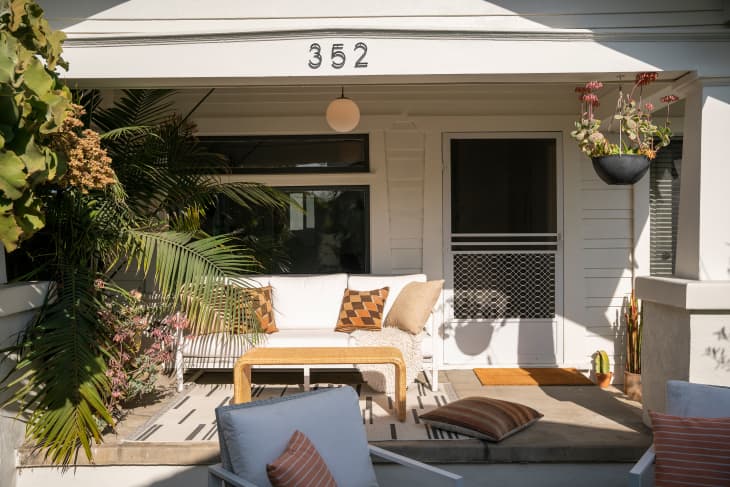 exterior of home: porch with white cushioned loveseat, large palm tree, hanging succulents