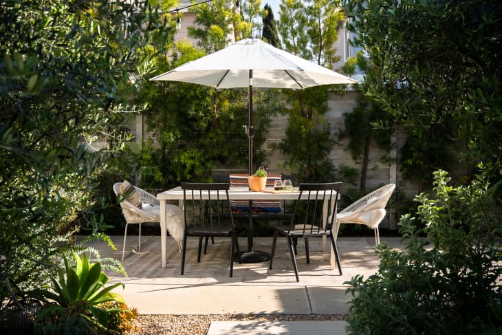 exterior of home: patio with white table, umbrella, white and black chairs, lots of trees and greenery