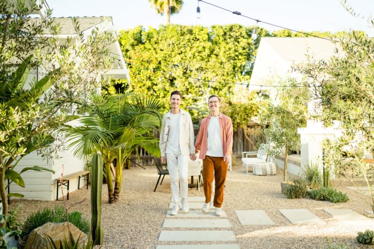 Two men holding hands walking in a nicely landscaped California yard.