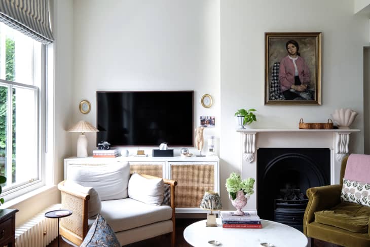 Vintage painted portrait mounted above fireplace in living room with mix match vintage arm chairs and caned white framed media console.