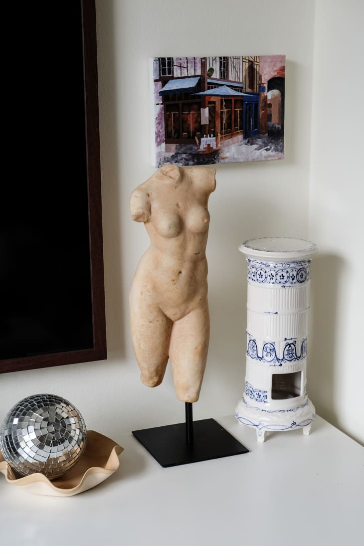 Body sculpture sits on table top surrounded by small disco ball and candle holder.