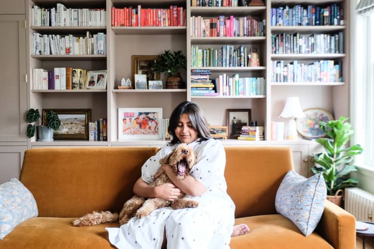Dweller hugging dog on ochre velvet sofa in book filled living room.