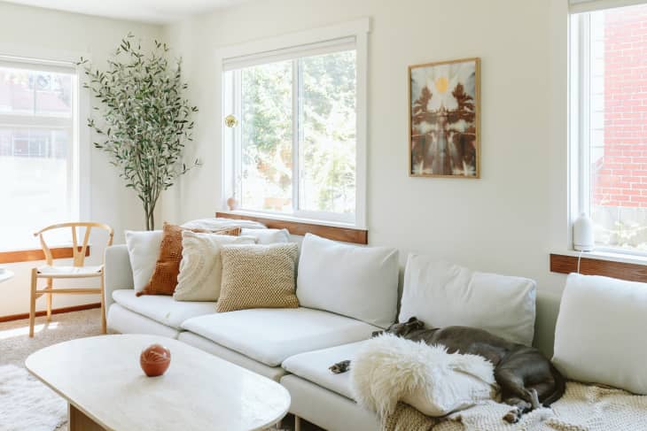 An oversized white couch with decorative pillows in a white living room as a dog naps on it.