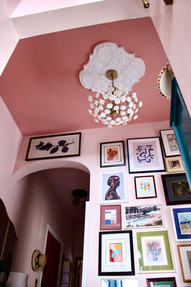 White floral chandelier mounted on pink painted ceiling. Gallery wall in hallway.