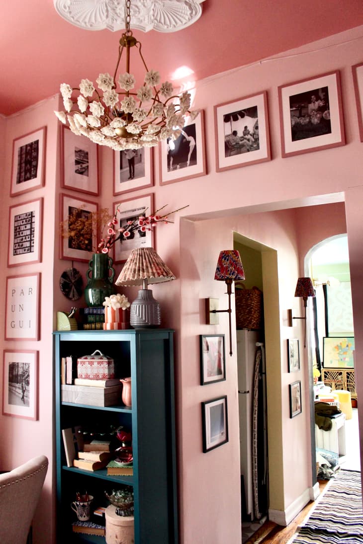 Floral chandelier hangs in pink painted office with photographs framed around the wall.