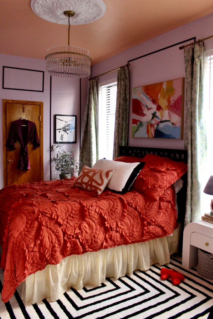 Burnt orange duvet on neatly made bed in purple painted bedroom.