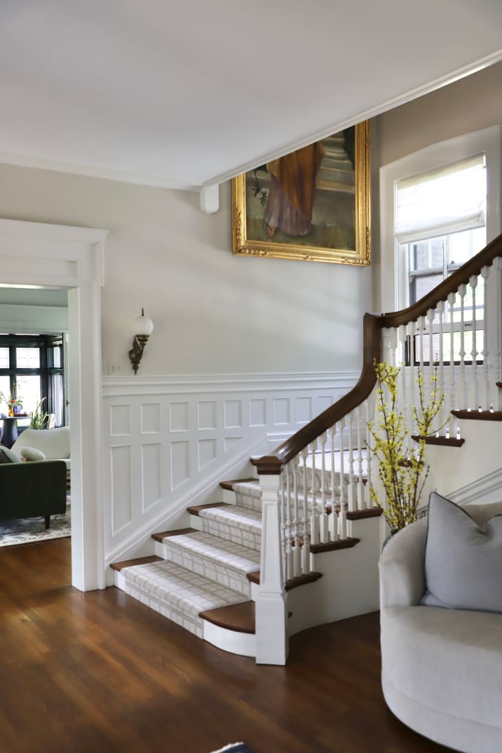 Neutral painted entry room with white wainscoting leading up the stairs.